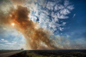 Smoke rising against the sun from controlled prairie burn